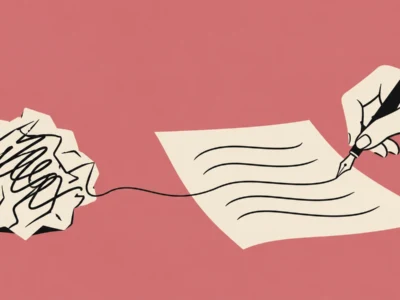 Hand with a fountain pen writing on a sheet of paper; a crumpled draft sits to the left.