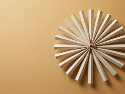 White radial paper fan sculpture forming a circular starburst on a warm beige background.