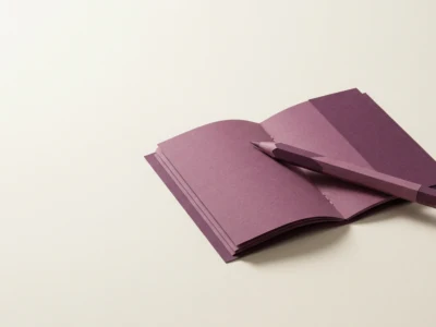Open purple notebook with a matching purple pencil resting on its pages on a pale beige background.