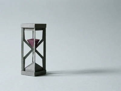 Miniature gray wooden hourglass with purple sand inside, placed on a light gray surface.