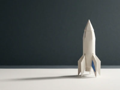 Elon Musk a sztuczna inteligencja od OpenAI do xAI i Groka - Promptowy White paper origami rocket standing on a white surface with a dark background, a minimalist setup.