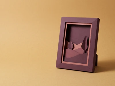 Papercut-style diorama with layered purple hills and a tree inside a tilted purple frame on a warm yellow background.