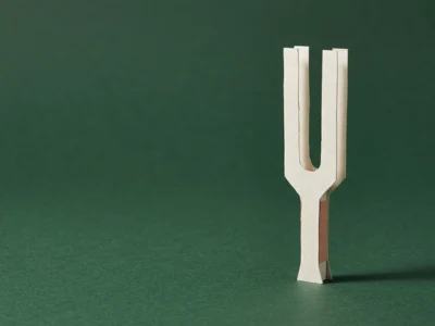 A small wooden U-shaped object standing upright on a green surface, casting a shadow to the right.