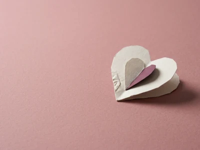 Layered paper hearts (white and pink) stacked on a soft pink background, symbolizing love or Valentine’s theme.