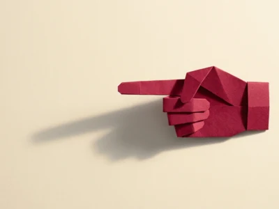 Red origami hand with index finger pointing to the left on a beige background, with a soft shadow