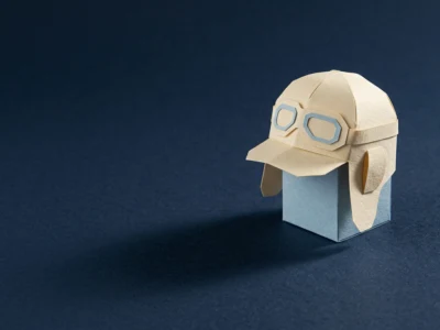 Paper craft helmet with blue-goggled lenses, placed on a pale blue block against a dark blue background.