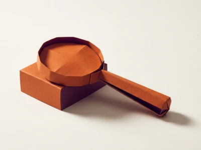 Orange paper origami object resembling a magnifying glass resting on a matching rectangular box.