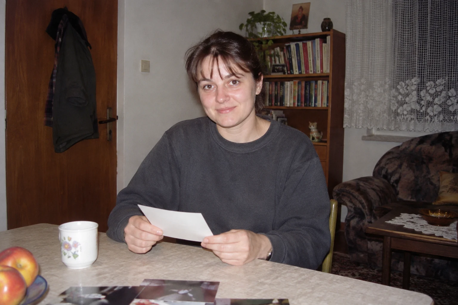 Kobieta z luźną odbitką przy stole w niewielkim pokoju, oświetlona prostym fleszem