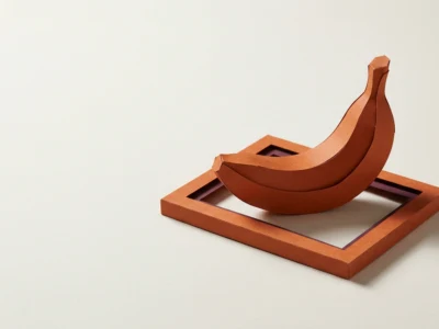 Orange paper sculpture of a banana placed across an orange rectangular frame with a purple inner edge on a pale surface, a minimalist still life.