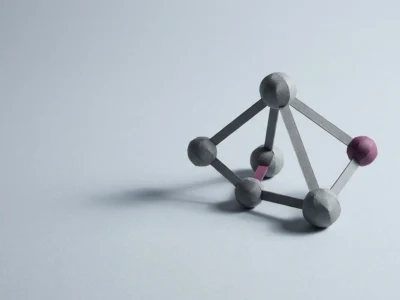 Wooden molecular model: gray spheres connected by rods forming a small tetrahedral cluster, with pink and purple end spheres.