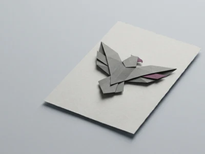 Origami bird folded from gray paper placed on a white card on a light gray surface.