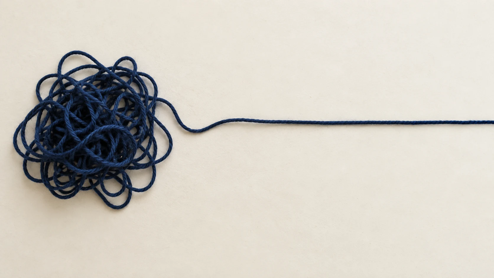 Blue tangled ball of string with a single long strand extending to the right on a light background.