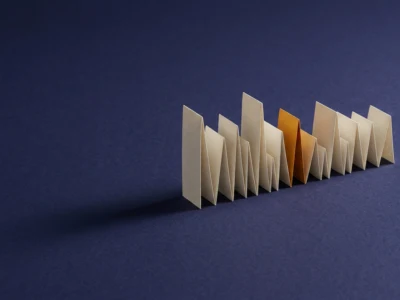 Row of white folded cards standing upright with a single brown card as the outlier on a dark blue background.