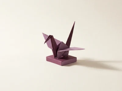 Purple origami crane on a small rectangular base, casting a shadow on a pale beige background.