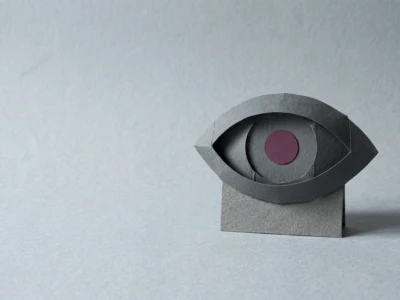 Abstract paper sculpture of a gray eye with a purple pupil on a small pedestal.