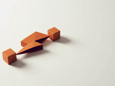 Orange origami cubes connected by a folded strip on a pale background, forming a short chain arrangement on white surface